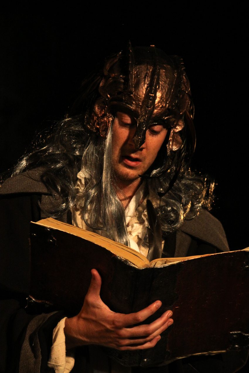 The Tempest, masked performer reading from a book